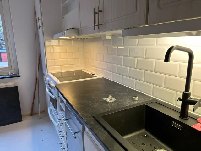 Kök med vitt kakel, svart bänkskiva och belysning under skåpen